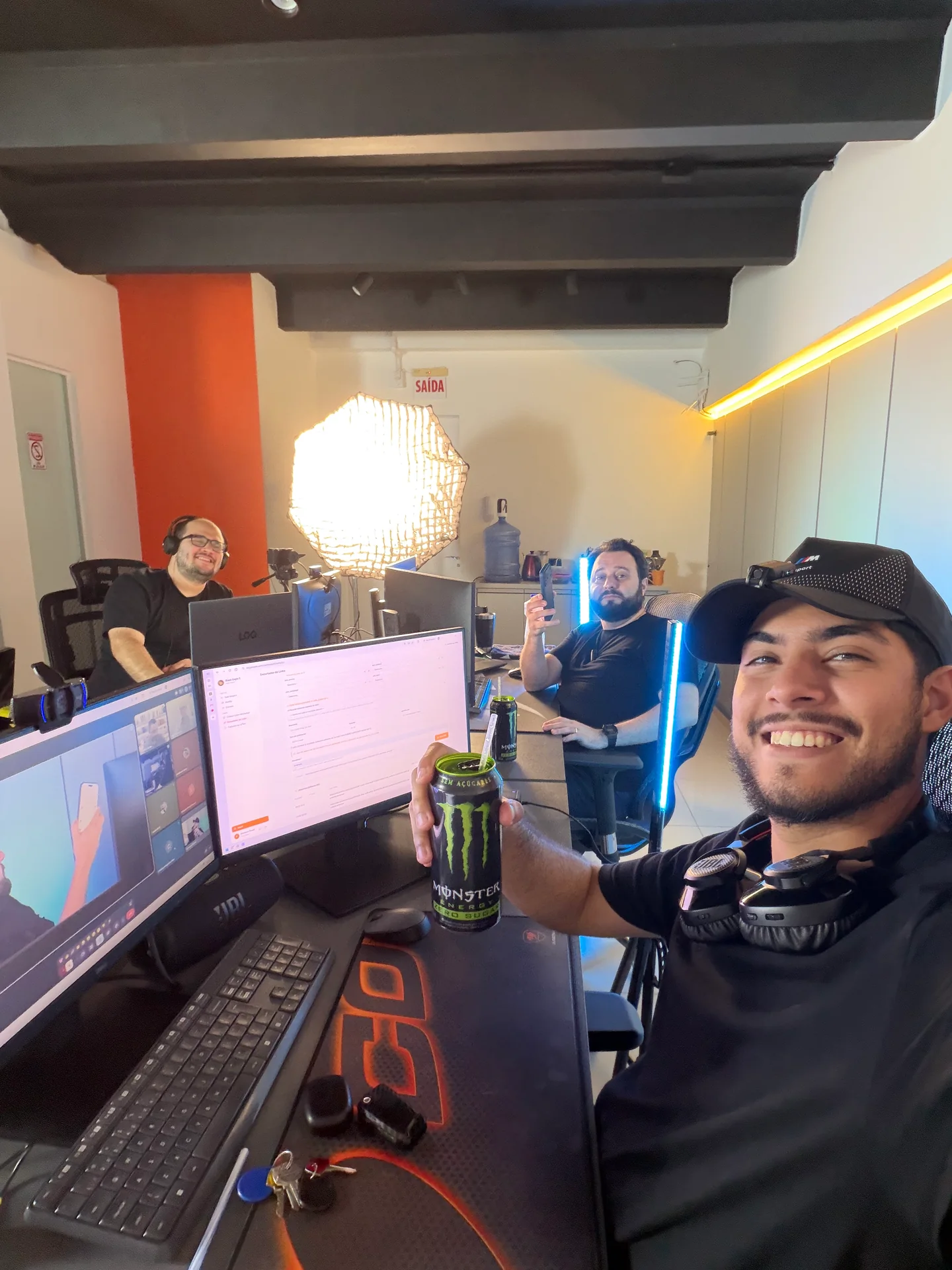 Foto coletiva e descontraída nos bastidores do estúdio, entre câmeras e mesas de trabalho.