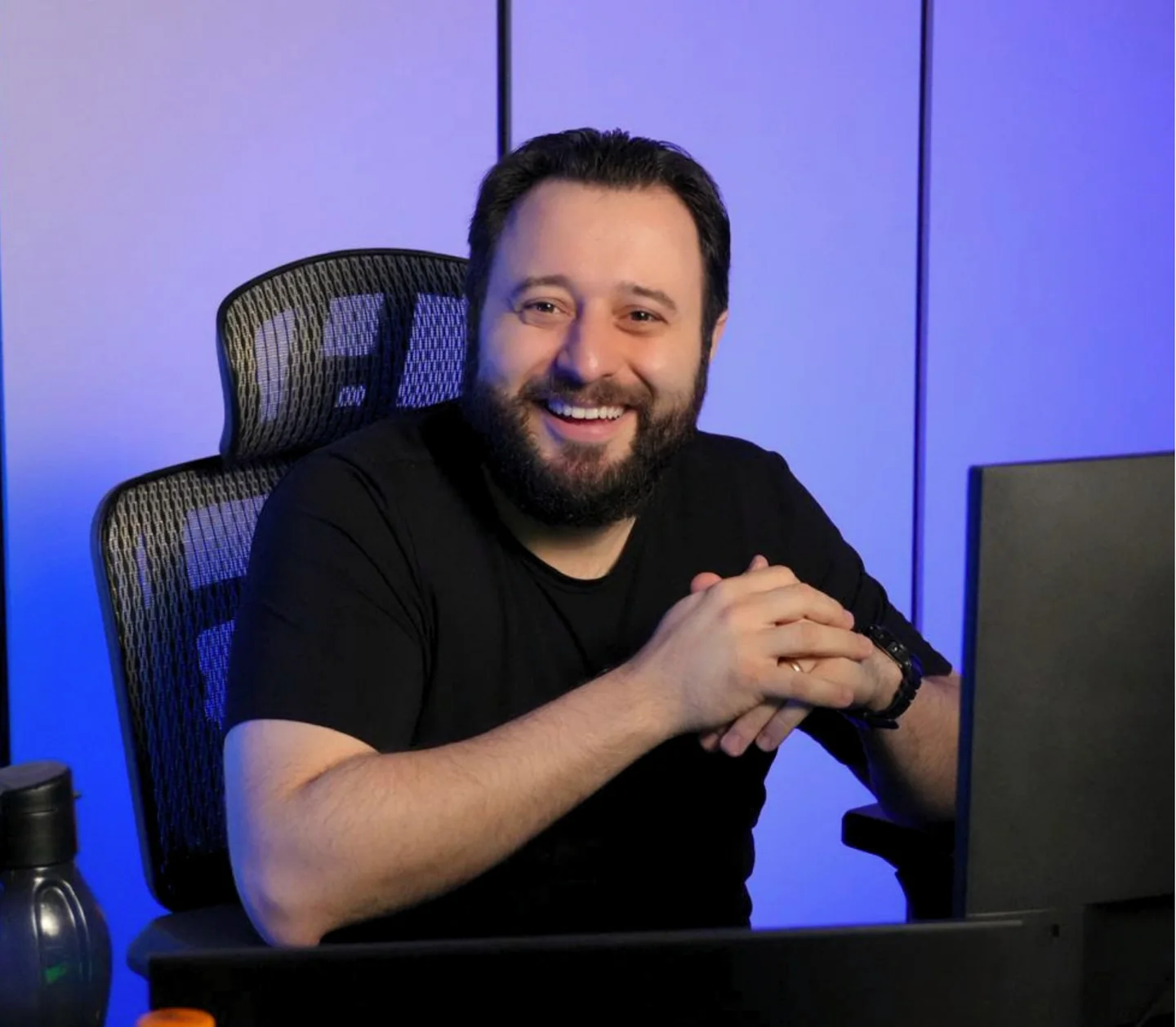 Joviano sorrindo, sentado à mesa do estúdio.