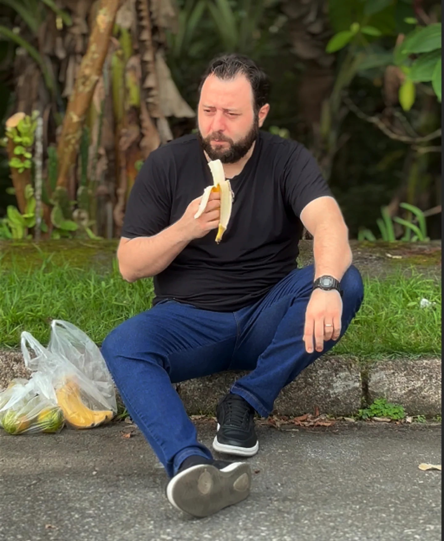 Joviano sentado ao ar livre, comendo uma banana.